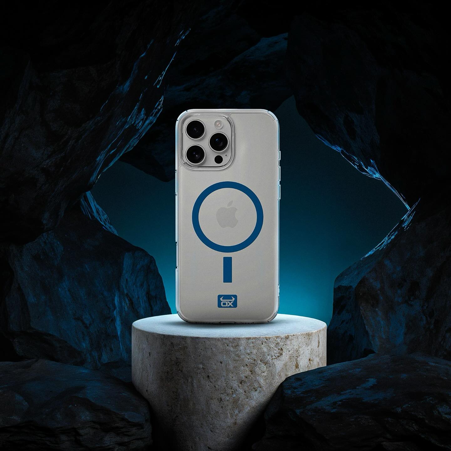 A clear phone case with a blue circular MagSafe ring and a small blue logo near the bottom, shown on a phone standing on a stone pedestal in a dark cave-like setting with blue lighting.